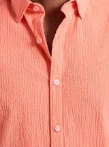 Close-up of a person wearing a pink textured shirt with buttons.