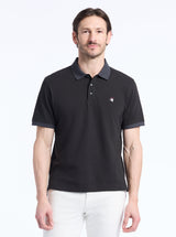 Man wearing a black polo shirt with a small devil logo on a white background