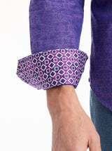 Close-up of a person wearing a purple patterned shirt with rolled-up sleeves on a white background