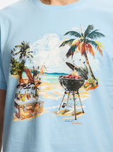 Light blue t-shirt with a beach scene graphic featuring a grill drinks, and palm trees.