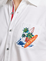 White shirt with a colorful pocket design featuring palm trees and surfboards.