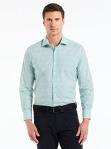 Man wearing a light blue patterned shirt and dark pants on a white background