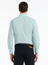 Man wearing a light blue patterned shirt and dark pants on a white background