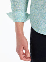 Close-up of a person wearing a light blue floral-patterned shirt with rolled-up sleeves on a white background.