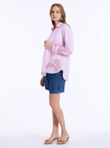 Woman wearing a pink blouse with floral embroidery and denim shorts on a white background